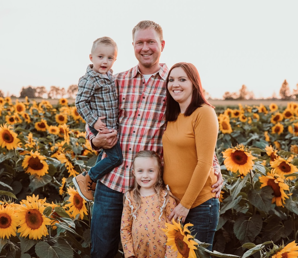 adam, kayla and kids stand in a field of sunflowers